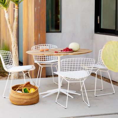 Outdoor dining scene with wooden table and white chairs on a patio.